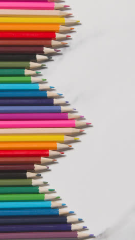 Vertical-Video-Of-Coloured-Pencils-Arranged-In-A-Symmetrical-Pattern-On-White-Marble-Background-